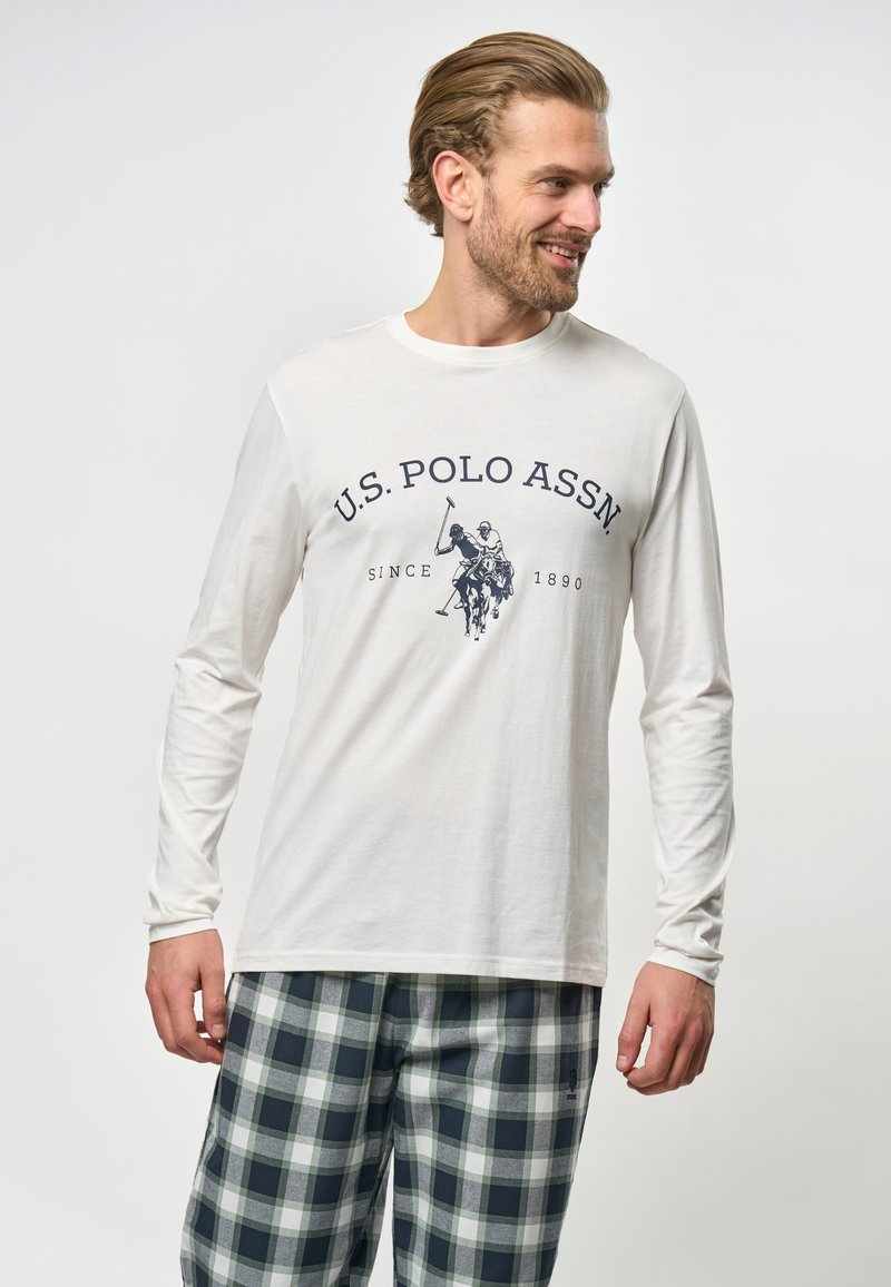 Hosszú ujjú fehér póló, tengerészkék nyomattal, amelyen az "U.S. POLO ASSN" felirat és egy pólós játékos grafika található, kockás tengerészkék és szürke nadrággal párosítva.