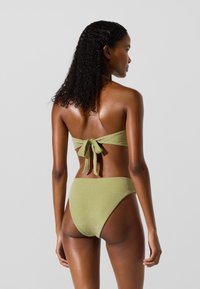 Zelený bikiny set s textúrovaným, lesklým povrchom. Horná časť má zaväzovanie na chrbte; spodná časť má vysoký strih nohavičiek a stredné pokrytie.