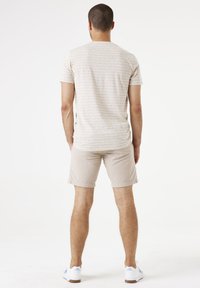 Camiseta de manga corta a rayas beige con cuello redondo, combinada con shorts beige claros, usados con zapatillas blancas sobre un fondo liso.
