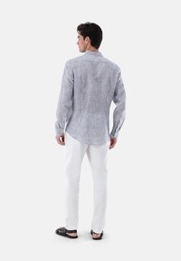 Camicia a righe a maniche lunghe blu e bianca, con colletto e polsini button-down, abbinata a pantaloni bianchi e sandali neri.