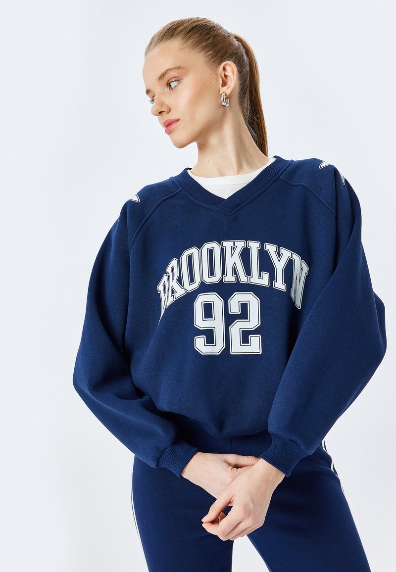 Granatowy sweatshirt z białym nadrukiem "BROOKLYN 92". Posiada dekolt w serek, długie rękawy oraz ściągacze na mankietach, wykonany z miękkiego materiału.