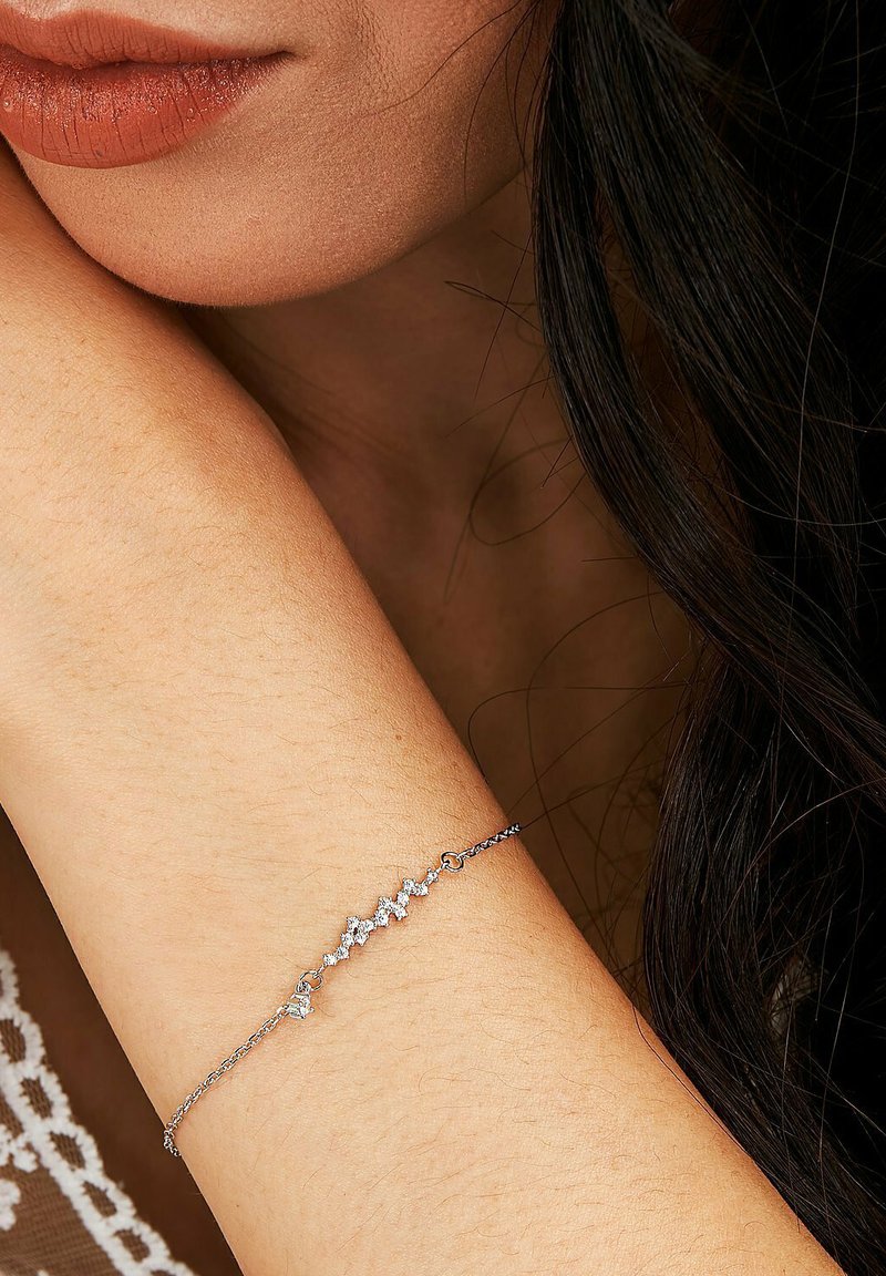 Silverkedjaarmband med flera små, klara ädelstenar arrangerade i ett zigzag-mönster på ett hudfärgat handled.