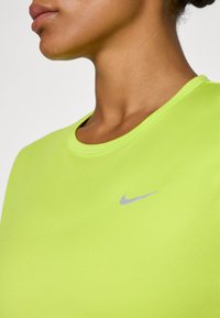Jasnozielona koszulka sportowa z okrągłym dekoltem i krótkimi rękawami, z małym szarym logo Nike na klatce piersiowej. Gładka struktura materiału.