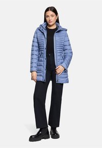 Jasnoniebieska puchowa kurtka z poziomym pikowaniem, zapinana na zamek, z bocznymi kieszeniami i kapturem. Połączona z czarnymi spodniami i botkami za kostkę.