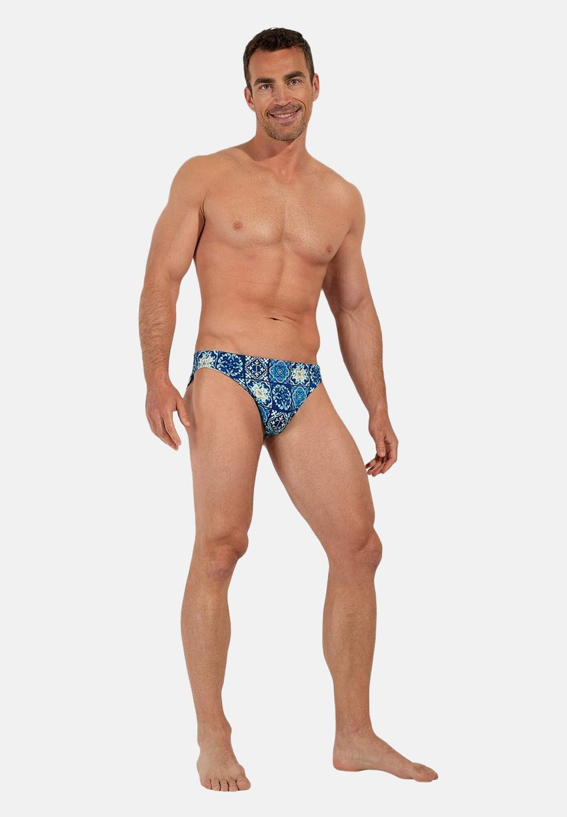 Slip de bain bleu et turquoise avec un motif géométrique. Le tissu semble doux avec une coupe ajustée et taille basse.