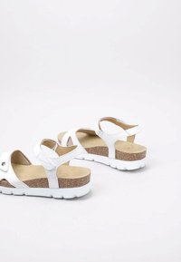 Witte sandalen met een kurken voetbed, verstelbare banden en een gestructureerde zool. Heeft een gladde faux leren bovenkant en contrasterende kurken accenten.