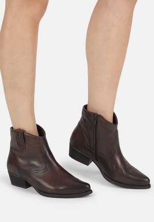 Brown leather ankle boots featuring a pointed toe, side zipper, and intricate embossed detailing on the front. Low stacked heel.