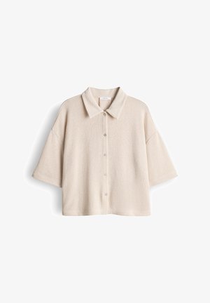 Beige overhemd met korte mouwen, knoopsluiting, kraag en losse pasvorm, afgebeeld tegen een witte achtergrond.
