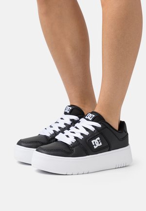 Black leather sneakers with white laces, textured surface, platform sole, and a prominent logo on the side. Casual and low-cut design.