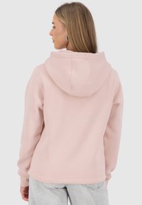 Felpa rosa con grande tasca posteriore e cappuccio con lacci. Tessuto morbido, polsini e orlo a coste. Indossata con jeans grigi chiari.