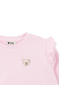 Top de color rosa claro con un patrón texturizado tipo gofre, que presenta mangas con volantes y un parche bordado de un oso en la parte frontal.