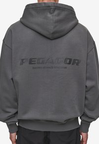 Grå överdimensionerad hoodie gjord av textilerat tyg. Har en stor huva, ribbade manschetter och "PEGADOR"-logotypen tvärs över ryggen i mörk tryck.