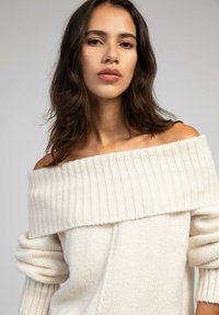 Pull crème décolleté avec un col côtelé et de longs poignets roulés. Texture douce avec un design ample et un détail de couture subtil.