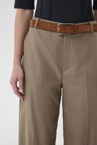 Beežid kohandatud püksid sileda tekstuuriga, millel on pruun seemisnahast vöö ja hõbedane metallkinnitus, osaliselt nähtav käsi küljel.