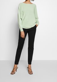 Suéter verde claro y holgado con un escote amplio; combinado con pantalones negros ajustados y tacones de tiras con estampado de animal.