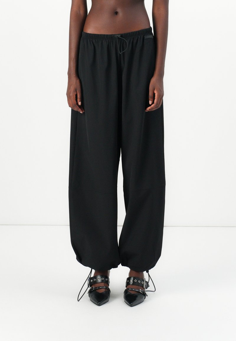 Pantalons noirs à jambes larges avec une taille élastique et un cordon de serrage. Le matériau semble léger, avec une texture lisse et des poignets froncés.