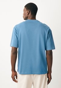 Világoskék pamut póló rövid ujjal, kerek nyakkivágással és laza szabással. A hátoldal egyszínű, minták nélküli.