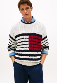 Μπλούζα με υφή και λαιμόκοψη τύπου crew-neck, με ρίγες σε λευκό, ναυτικό μπλε και κόκκινο. Πολύπλοκο σχέδιο πλεξίματος καλωδίωσης, με έντονη κόκκινη μπλοκαρισμένη περιοχή. Φορεμένη πάνω από πουκάμισο.