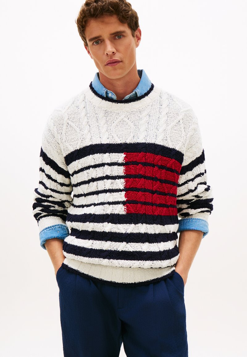 Μπλούζα με υφή και λαιμόκοψη τύπου crew-neck, με ρίγες σε λευκό, ναυτικό μπλε και κόκκινο. Πολύπλοκο σχέδιο πλεξίματος καλωδίωσης, με έντονη κόκκινη μπλοκαρισμένη περιοχή. Φορεμένη πάνω από πουκάμισο.