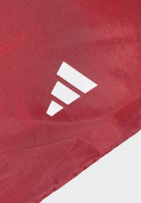 Sac rouge avec une texture lisse, arborant un logo en trois bandes blanches dans le coin inférieur droit, soulignant la simplicité du design.