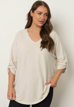 Maglione beige chiaro con scollo a V, maniche lunghe e polsini arrotolati. Presenta un motivo a righe textured e tasche laterali.