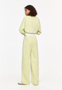 Hellgrüner oversized Pullover mit Ballonärmeln, weißem Bund und passenden weiten Hosen aus weichem Stoff. Weiße Schuhe sind sichtbar.