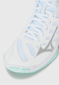 Chaussure de sport blanche avec des inserts en maille bleu clair. Présente des accents argentés et une semelle texturée en vert menthe. Conception à lacets.
