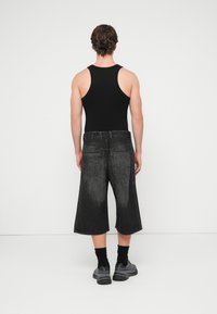 Μαύρο αμάνικο τοπ σε συνδυασμό με ξεβαμμένα μαύρα σορτς από τζιν μέχρι το γόνατο. Τα σορτς έχουν άνετη εφαρμογή και πίσω τσέπες, φορεμένα με μαύρες κάλτσες και αθλητικά παπούτσια.