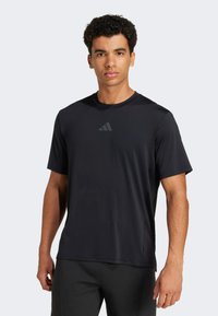 Camiseta atlética negra de manga corta, fabricada con tejido que absorbe la humedad, con cuello redondo y un logo sutil en el pecho; textura suave.