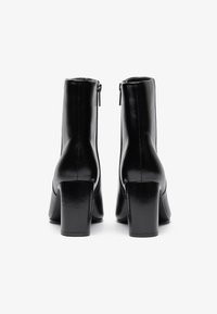 Black leather ankle boots with a smooth finish, square heels, and side zippers, showcasing a sleek silhouette and minimalistic design.