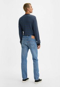 Camisa de manga larga a rayas en azul marino y negro, jeans de mezclilla azul y zapatillas negras. Parche de cuero visible en la cinturilla trasera de los jeans.