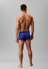 Boxer-briefs bleus avec un logo Calvin Klein noir sur la ceinture, design ajusté, texture douce et tissu lisse.