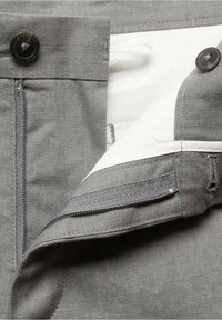 Pantalons en tissu gris avec fermeture éclair, deux boutons à la taille et doublure blanche avec des détails de couture raffinés.