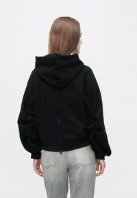 Μαύρο φούτερ με κουκούλα και φερμουάρ, φουσκωτά μανίκια και cropped σχεδιασμό. Διαθέτει απαλή υφή και απλή, καθαρή σιλουέτα.