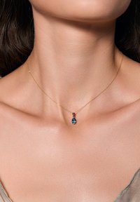 Złoty łańcuszek z owalnym wisiorkiem z turkusu, z gładką powierzchnią i delikatnym zapięciem, leżący na nagiej skórze.