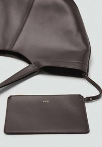 Sac à main en cuir marron avec une texture lisse et un portefeuille intégré. Le portefeuille présente un logo doré et une fermeture éclair. Design simple et minimaliste.