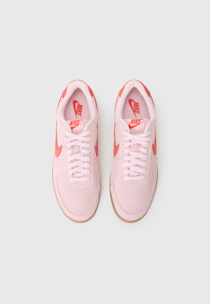 Sneakers in suede rosa con dettagli rossi, dotati di allacciatura tradizionale, suola in gomma e iconico marchio Nike sulla linguetta e sul lato.