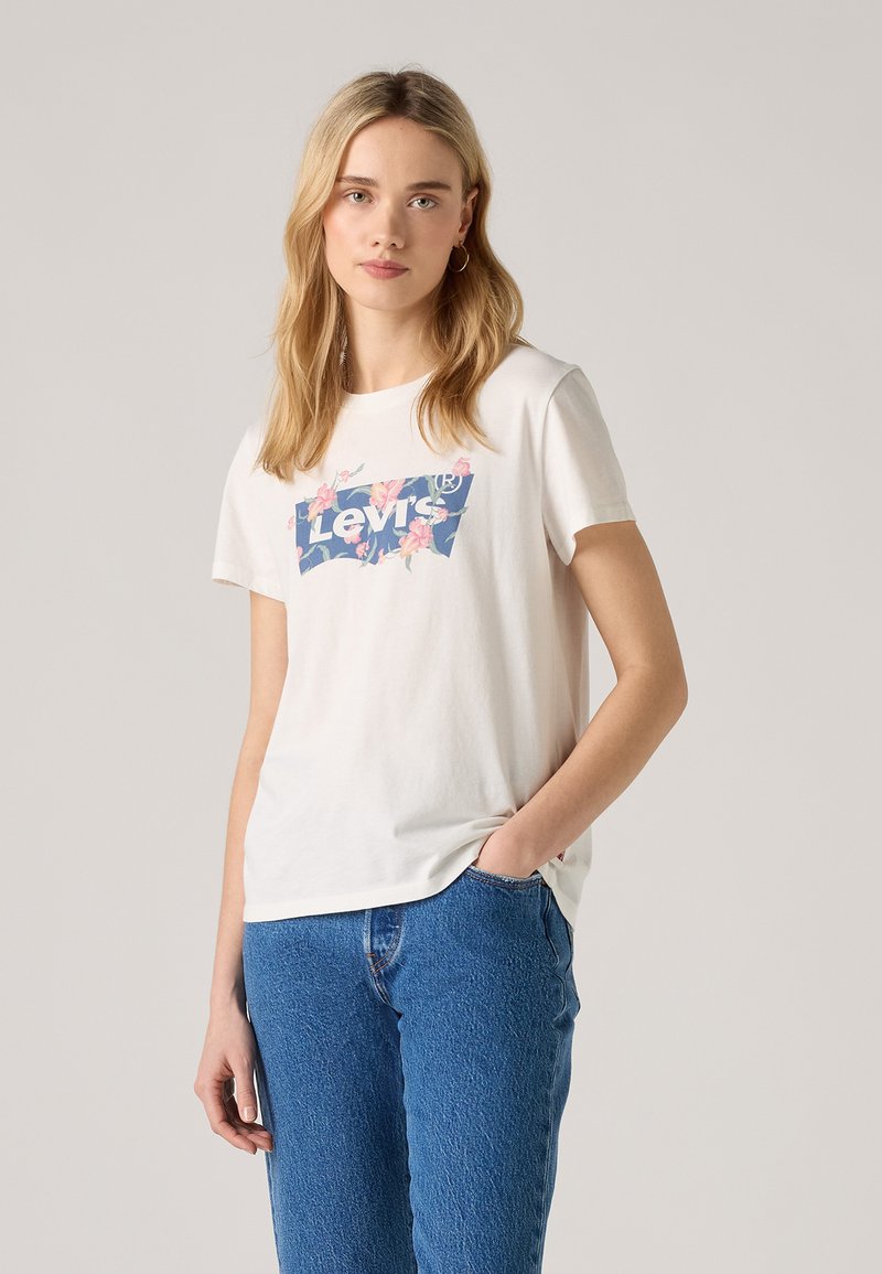 Biela bavlnená tričko s modrou kvetinovou grafikou loga Levi's. Krátke rukávy a voľný strih. Nosené s modrými džínsami.