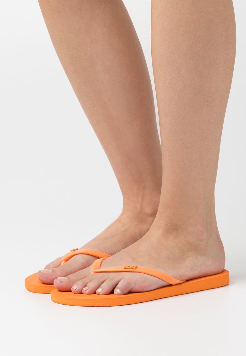 Tongs orange en caoutchouc, dotées d'une bride en V simple et de semelles plates, avec une surface texturée pour une meilleure adhérence.
