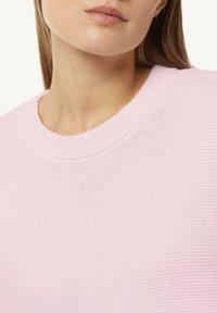 Jasnoróżowy sweter z dzianiny z okrągłym dekoltem. Materiał ma teksturowaną strukturę, jest lekki i ma miękkie wykończenie.