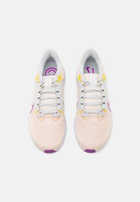 Zapatillas de malla rosa claro con cordones grises, acentos morados y detalles amarillos. Punta redonda y suela blanca acolchada. Superficie texturizada.
