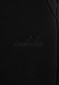 Zwarte stof met subtiele, geborduurde tekst "similodon" in cursieve stijl nabij de naad.