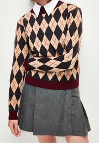Maglione a motivo argyle con colori beige, nero e bordeaux. Tessuto lavorato a maglia con polsini e collo a coste. Abbinato a una gonna grigia.