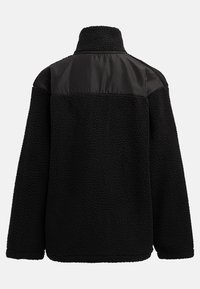 Mustat fleece-takit, joissa on korkea kaulus, tekstuuripinta ja kontrastiväriset sileät mustat kankaat olkapäissä. Ei näkyviä kiinnityksiä.