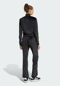 Černý sametový teplákový komplet s přiléhavým límcem a elastickými manžetami, s hladkým povrchem a volným střihem, doplněný černobílými teniskami.