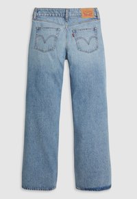 Jean en denim bleu clair avec une coupe large, coutures visibles, deux poches arrière avec un logo en forme de V et une étiquette en cuir de la marque sur la taille.