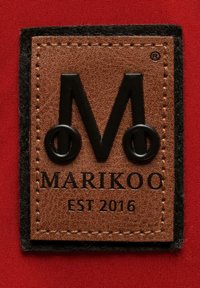 Bruin leren patch met zwarte geëmboste initialen "M", merknaam "MARIKOO" en "EST 2016", omrand door zwarte vilt, tegen een rode achtergrond.