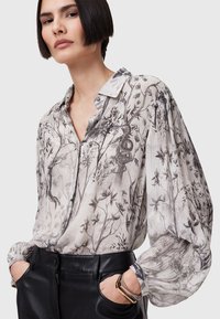 Let, semi-transparent bluse med et blomsteragtigt sort-hvidt mønster, knap-ned krave og voluminøse ærmer. Kombiner med sorte bukser.