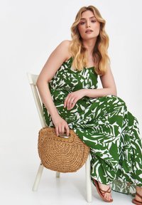 Maxikleid mit grün-weißem Blumenmuster, schicke Woven-Strohtasche mit Griff und braunen Sandalen. Glattes Gewebe mit sanftem Fall.