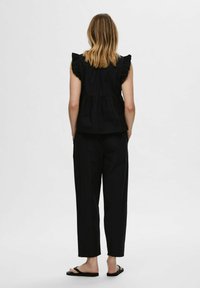 Črn peplum top s nabranimi rokavi v kombinaciji z ohlapnimi črnimi hlačami in ravnimi sandali. gladka tekstura, minimalističen dizajn.